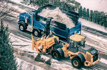 Souffleuse à neige déneigeant une route remplissant un camion